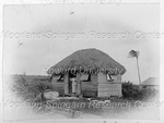 Woman Standing at the Door of a Residence with a Thatched Roof