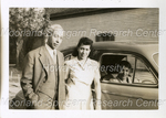 Unidentified Man and Woman Standing Next to an Automobile With an Older Woman inside