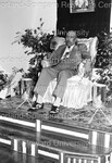 Sweet Daddy Grace seated on stage fanning himself; holding money by Harold Hargis