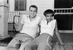 Man and Woman sitting on front porch of house by Harold Hargis