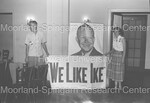 2 Unidentified people holding "We Like Ike" poster under a large photo of Dwight D. Eisenhower by Harold Hargis