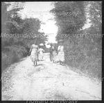 Four Women and One Man Walking Down a Dirt Road with Baskets on their Heads